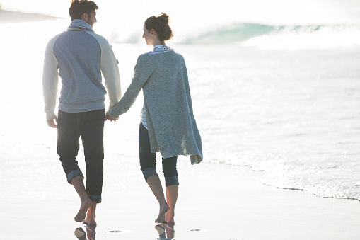 Rear view of a senior couple standing arm in arm together on a beach and looking out at the sunset over the ocean