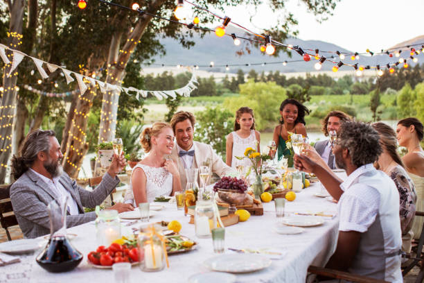 young couple and their guests sitting at table during wedding reception in garden - wedding champagne table wedding reception imagens e fotografias de stock