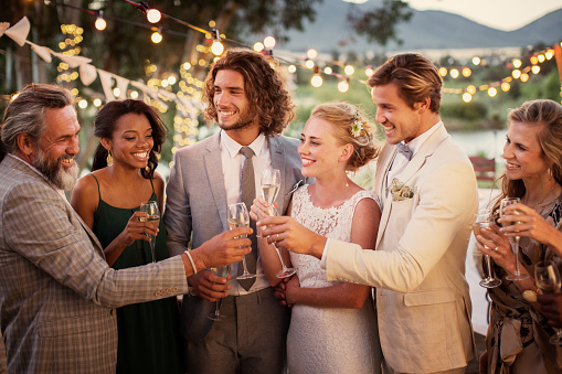 Pareja joven y sus invitados con flautas de champán durante la recepción de la boda en el jardín photo