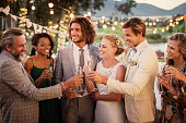 Young couple and their guests with champagne flutes during wedding reception in garden
