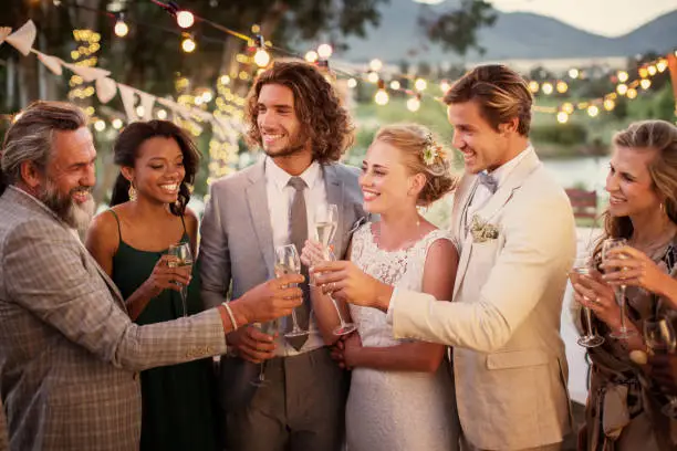 Photo of Young couple and their guests with champagne flutes during wedding reception in garden
