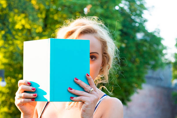 mujer joven se refugiaba detrás de un libro - outdoors book reading accessibility fotografías e imágenes de stock