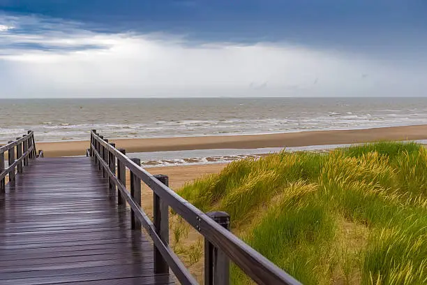 Wooden staircase leading into stormy sky and sea at De Haan, Belgium