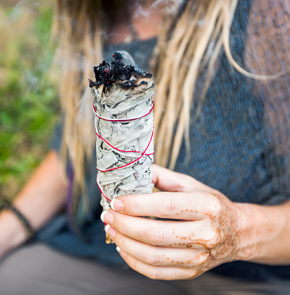 New age woman with dreads, sitting in nature burning sage