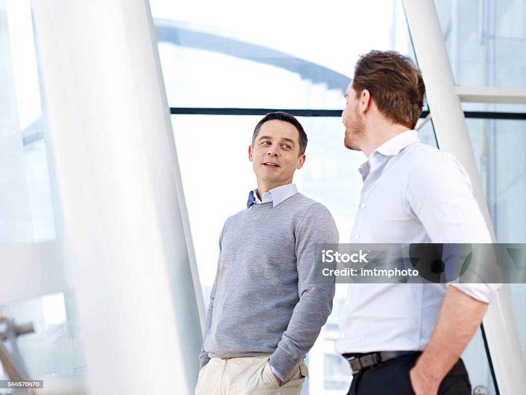 Hombres de negocios hablando frente a las ventanas en la oficina - Foto de stock de Cara a cara libre de derechos