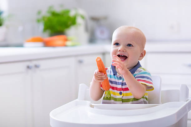 маленький ребенок ест морковь - baby carrot snack healthy eating small стоковые фото и изображения