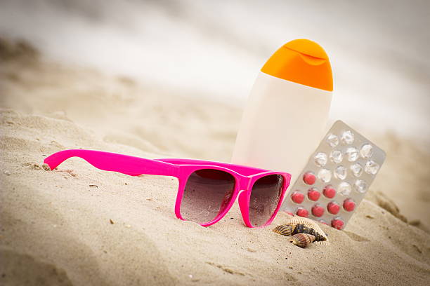 Pink sunglasses, shells, sun lotion, pills of vitamin E on sand at the beach, seasonal concept and successful tanning