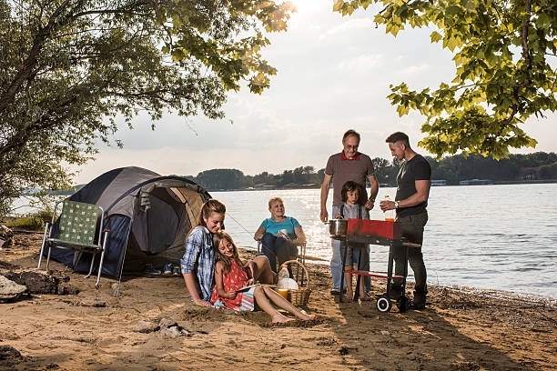 Extended family making barbecue during camping day by the river. Happy multi-generation family spending a day on the beach by the river and making barbecue. family bbq beach stock pictures, royalty-free photos & images