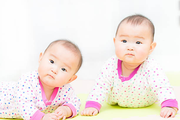 Two newborn twins are peacefully slumbering side by side, their heads touching softly. The calming atmosphere captures the pure bond they share in their early days of life.