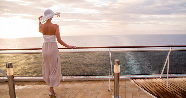 Female looking at sea while standing in cruise Rear view of young woman looking at sea. Female is standing at railing in cruise ship against sky. She is wearing white dress and sun hat. cruise ship stock pictures, royalty-free photos & images