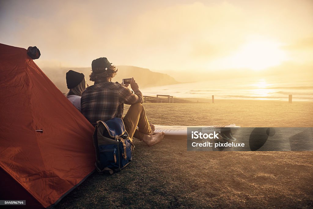 This is my kinda date! Shot of two surfers sitting by a tent while waiting for the perfect wave Camping Stock Photo