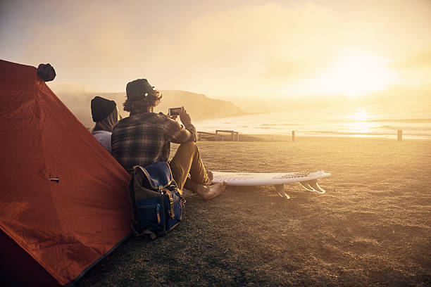 This is my kinda date! Shot of two surfers sitting by a tent while waiting for the perfect wave outdoor pursuit photos stock pictures, royalty-free photos & images