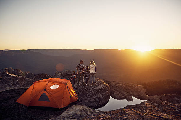 Young man and woman outside tent hiking on rugged terrain with mountains in the background.