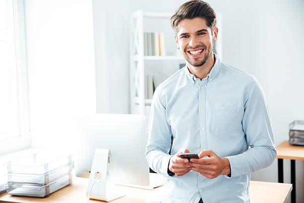 istock Smiling businessman standing and using mobile phone in office 544603476