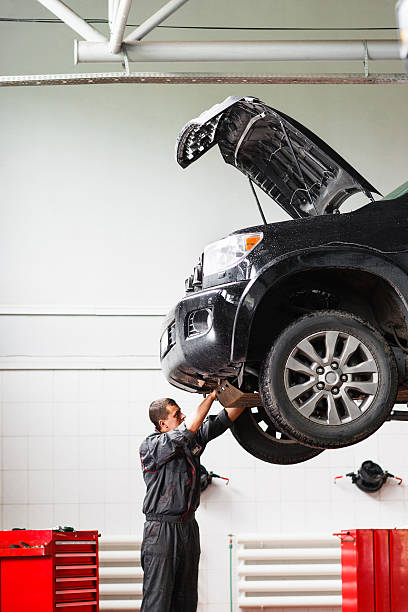 Mechanic working under car in service station Mechanic working under raised car in service station. Mechanic disassemble lifted on hoist car. Young male mechanic repairing SUV car in garage mechanic working under car stock pictures, royalty-free photos & images