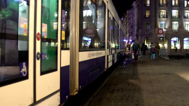 Modern tramcar leaving tram stop, active traffic in city downtown at night