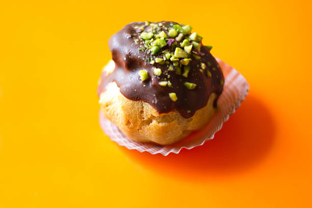 A pretty chocolate cream puff/eclair with pistachio sprinkles on a vibrant pink background. Copy space available.