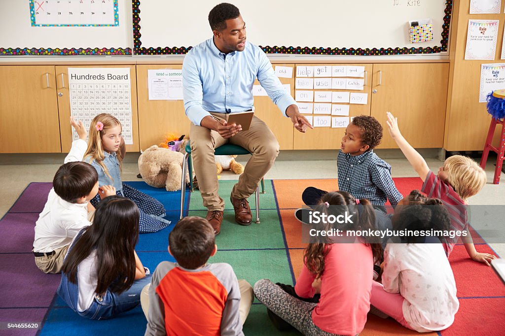 Elementary school kids sitting around teacher in a lesson Teacher Stock Photo