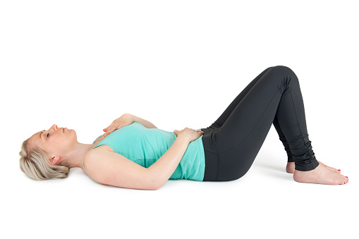 Full body view of a young blond woman in Yoga exercises against white background with light shadow
