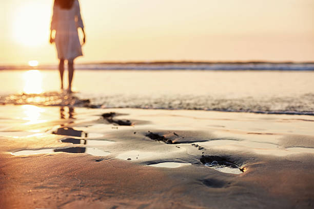 istock Footprints in sand with woman walking in background during sunse 544664540