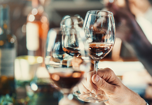 Closeup of group of unrecognizable people tasting different types of wines at a winery. Shallow focus, hands and glasses in the frame.