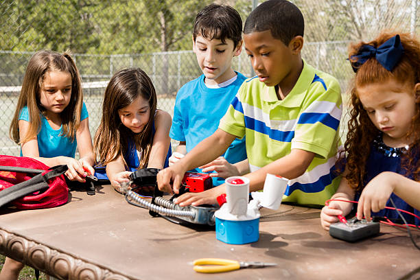 Little engineers! Multi-ethnic elementary children collaborate on 'robot' creation. Group of multi-ethnic, elementary age children collaborate on a 'robot' they created using tools, objects they found at home. Imagination, creativity, inspiration for these little engineers!  Park or schoolyard setting. school science project stock pictures, royalty-free photos & images