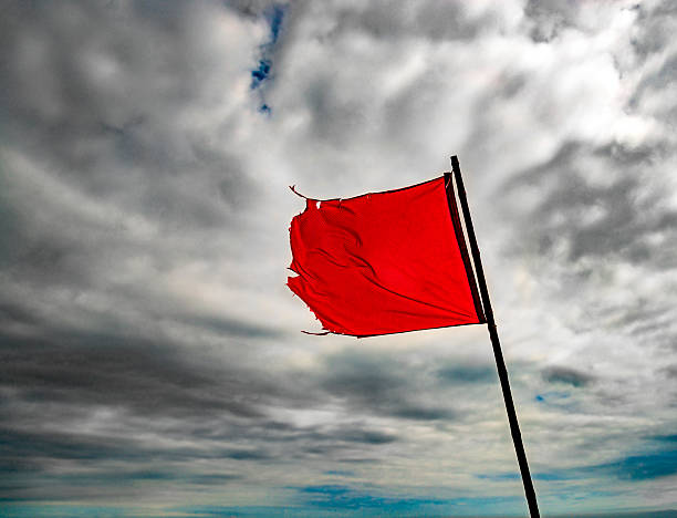 Torn, red warning flag flying under grey skies stock photo