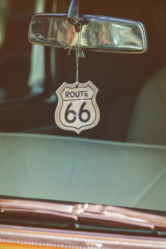 Retro styled image of a Route 66 badge hanging on a car mirror of a classic car