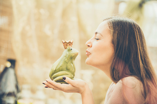 Woman trying to kiss a ceramic - ornamental frog