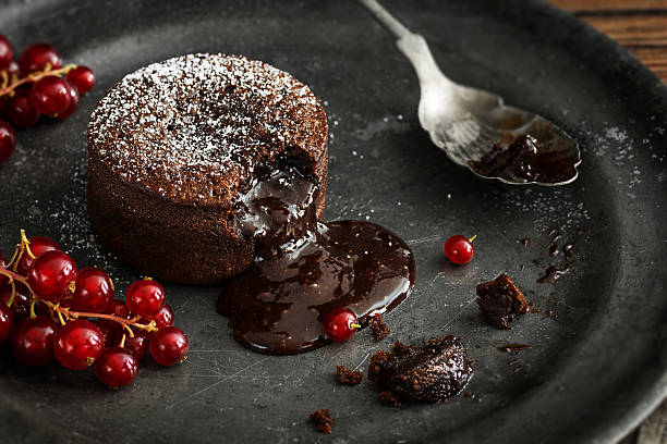 Warm Chocolate Lava Cake with Molten Center and Red Currants A single serving of warm chocolate lava cake sprinkled with powdered sugar with a bite taken out. The molten chocolate center spills out through the hole in the cakey wall. Red currant berries are the garnish for this indulgent dessert on a vintage metal plate. dessert sweet food stock pictures, royalty-free photos & images