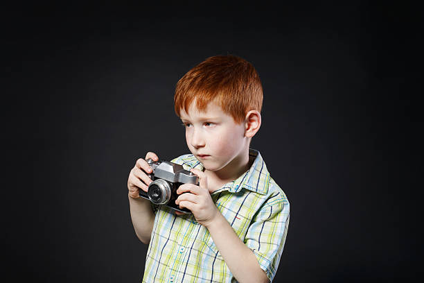 il bambino scatta foto con una fotocamera vintage su sfondo nero - fashionable studio shot indoors lifestyles foto e immagini stock