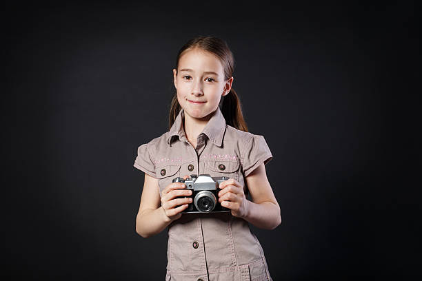 la bambina scatta foto con fotocamera vintage su sfondo nero - fashionable studio shot indoors lifestyles foto e immagini stock