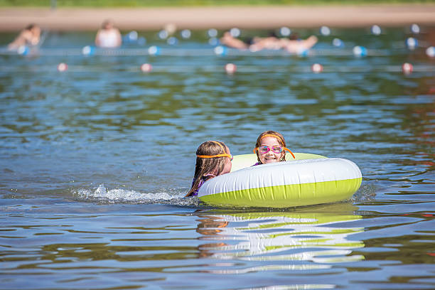 две молодые девушки, играя с внутренней пробирку на озеро - inner tube swimming lake water стоковые фото и изображения