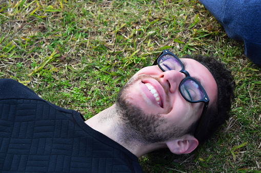Closeup of young latin man relaxing on the grass. Happy man resting outside.