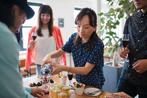 Woman pouring red wine into a friends glass at a dinner party. Kyoto, Japan. May 2016
