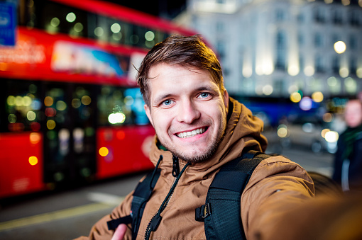 Young hipster man walking in the streets of London at night, taking selfie