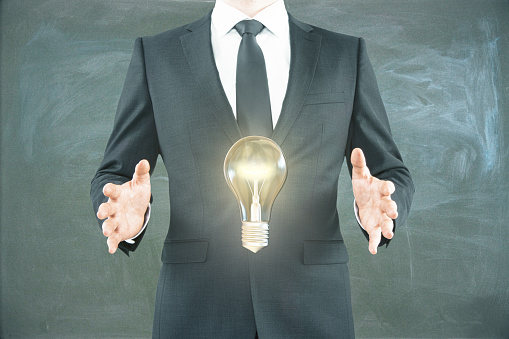 Idea concept with businessman holding levitating lightbulb on chalkboard background