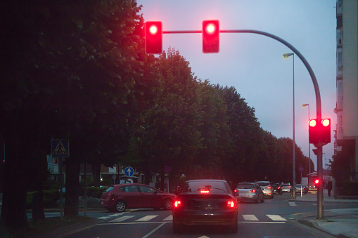 Street view , red traffic and car lights in the foreground, city life, row of cars and trees.