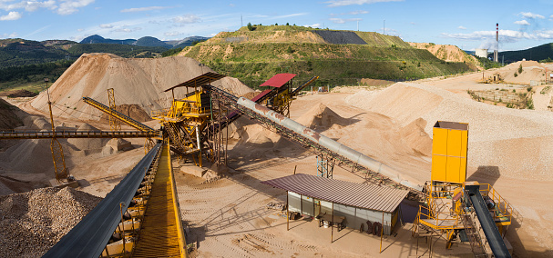 Panoramic gravel pit in mountain area with machinery and distribution tapes gravel according sizes, lots of gravel and sand for construction industry. We also see debris storage terraces or waste coal power plant in the background - Panoramic view of gravel in mountain area with machinery and gravel distribution tapes according to sizes, with piles of gravel and sand for the construction industry. We also see storage terraces for debris or waste from coal power plant in the background