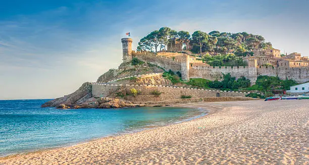 View of the fortified walls of the Vila Vella of Tossa de Mar from the beach. The only example of a medieval town still standing on the Catalan coast. It still has the entire original perimeter with battlemented stone walls, four turrets and three cylindrical towers with parapets. The interior of the Old Town is a charming place with narrow, cobblestoned streets, the Governor's House, a medieval hospital, and remnants of a Romanesque church and a Gothic church. Tossa de Mar, Costa Brava, Catalonia, Spain