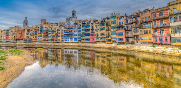 Colorful river-front houses of all shapes and sizes, painted in various ochre, yellow and red tones lining the Onyar river. Girona,