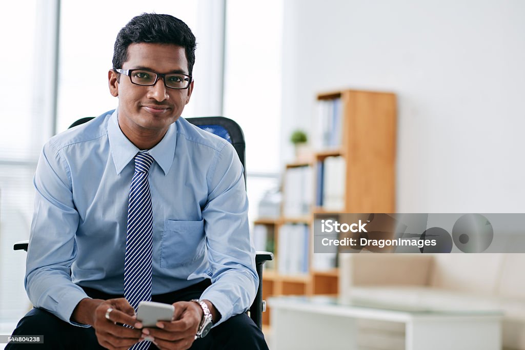Businessman with smartphone Portrait of smiling Indian business person with smartphone sitting in office Culture of India Stock Photo