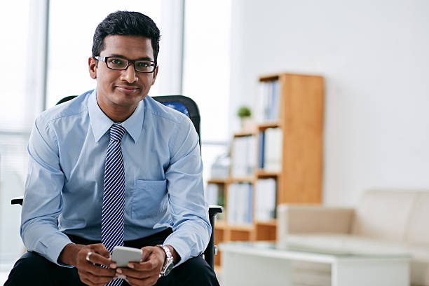 Businessman with smartphone Portrait of smiling Indian business person with smartphone sitting in office culture of india stock pictures, royalty-free photos & images