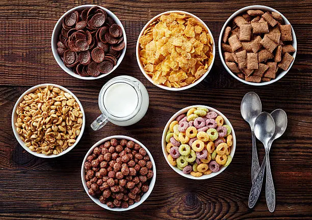 Bowls of various cereals and milk from top view