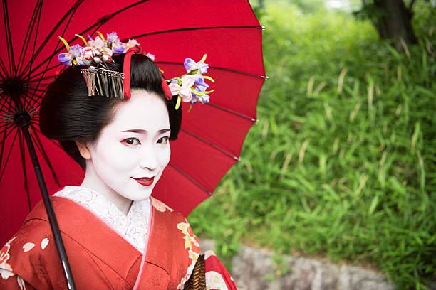 istock Japanese geisha under red parasol, smiling towards camera 544806864