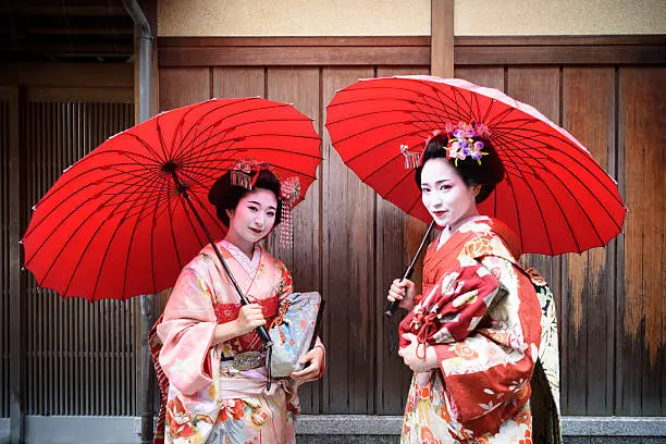 Two young women holding parasols wearing traditional maiko kimonos