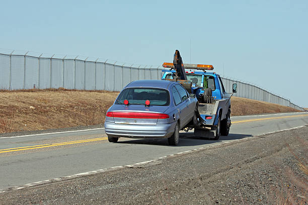 Tow Truck Towing A Vehicle On A Two Lane Highway Rear quarter view of a tow truck towing a broken down, nondescript, older model vehicle on a secondary highway. towing photos stock pictures, royalty-free photos & images