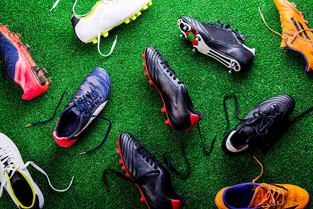 Unrecognizable little football player against green grass, studi Unrecognizable little football player with soccer ball tying shoelaces, against artificial grass. Studio shot on green grass. cleats stock pictures, royalty-free photos & images