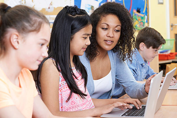 teacher helping group of elementary school children in computer - teacher computer high school student classroom imagens e fotografias de stock