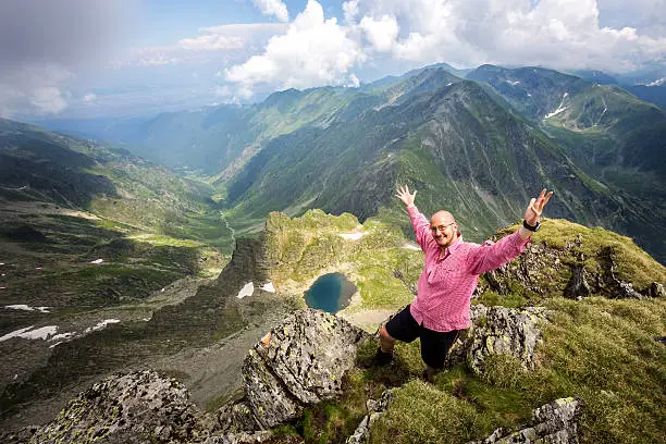 Young, extreme, active hiker fealing happy on top of the Lespez peak in the Carpathian mountains after a healthy successful hike with cloudy sky and the green valley of Laita in the background.